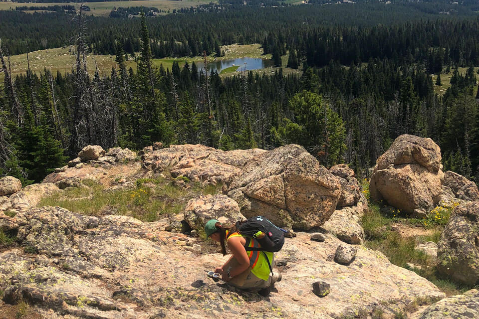 Student kneels on a cliff.